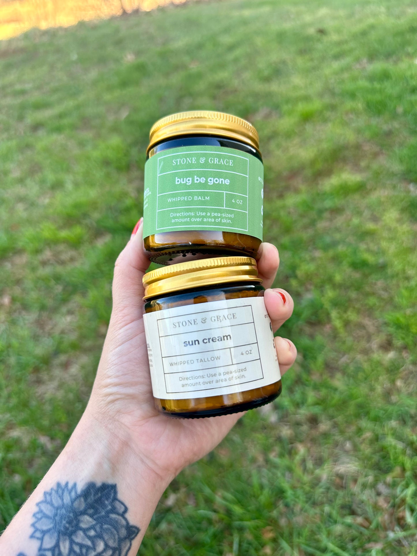 Hand holding two jars of Stone & Grace skincare products against a grassy background