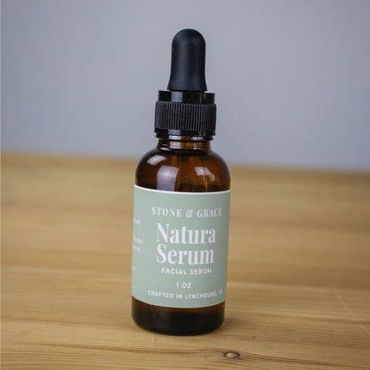 Bottle of Stone & Grace Natura Serum on a wooden surface with a gray background