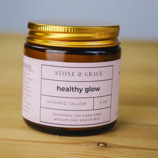 Jar of 'healthy glow' whipped tallow from Stone & Grace on a wooden surface.