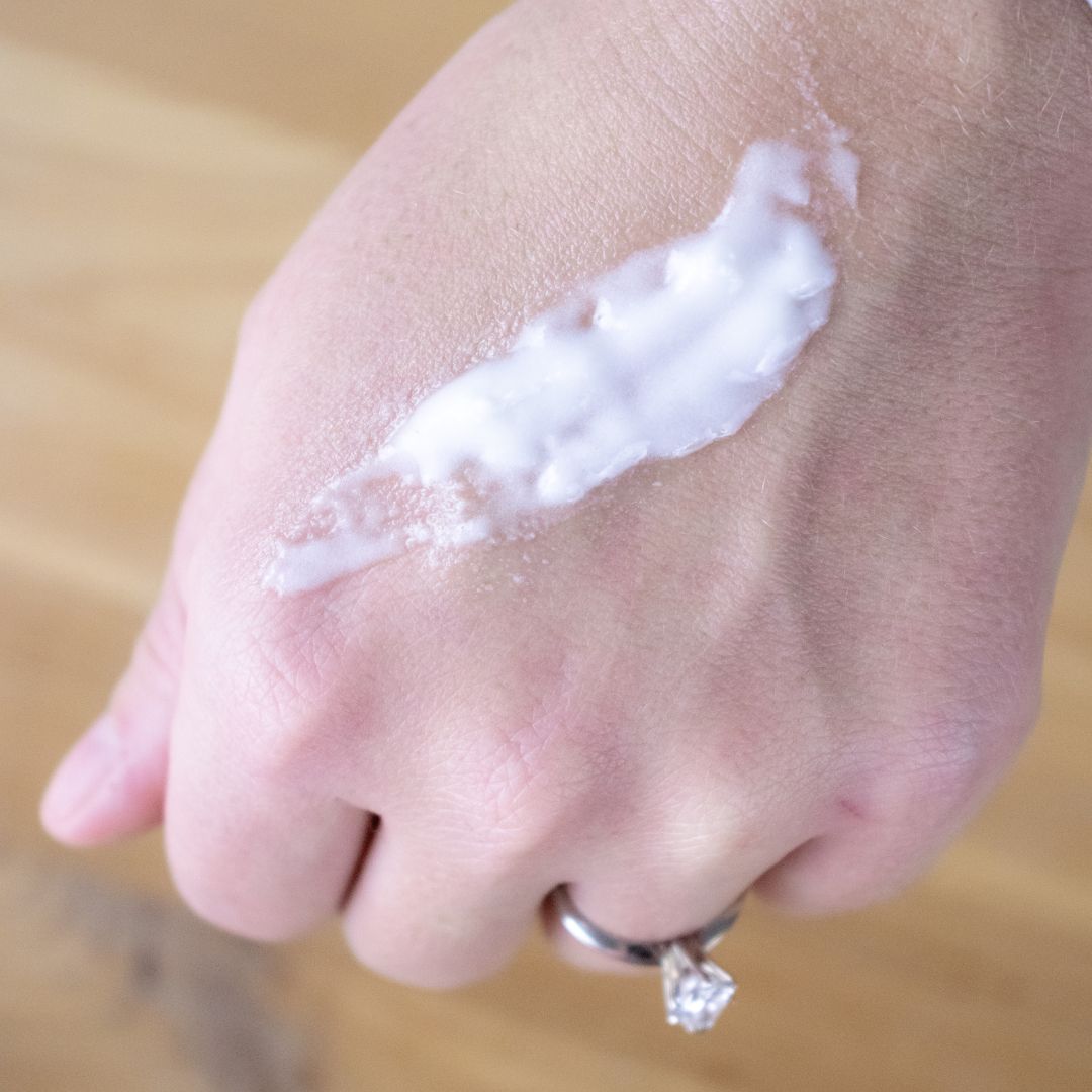 Hand with a small amount of white cream on the back of a hand against a blurred background