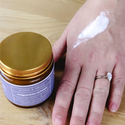 Jar of cream with gold lid and purple label next to a hand with cream on a wooden surface