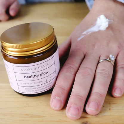 Jar of 'Healthy Glow' cream with a hand applying cream on a wooden surface