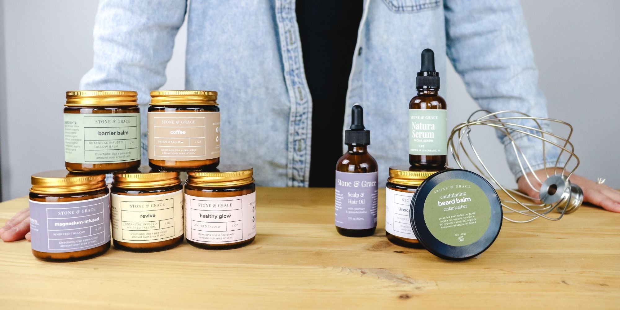 Collection of skincare products including jars and bottles by Stone & Grace on a wooden surface with a person standing in the background.
