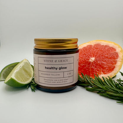 Jar of 'Healthy Glow' product by Stone & Grace with citrus fruits and rosemary on a white background #healthyglow #tallow #grassfedtallow #naturalskincare #tallowskincare #tallowskin #rosemary #skincare #moisturizer #naturalmoisturizer