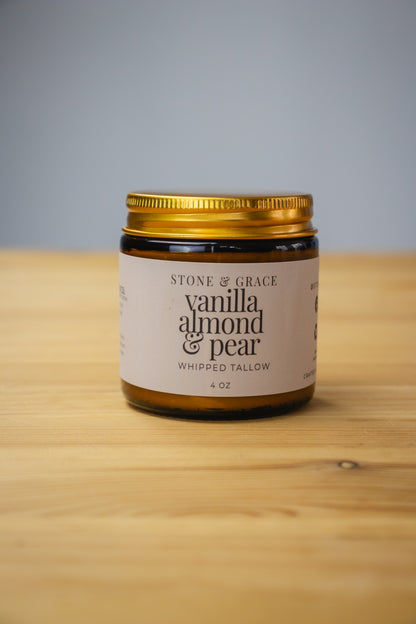 Jar of 'Vanilla Almond Pear' whipped tallow from Stone & Grace on a wooden surface with a gray background.