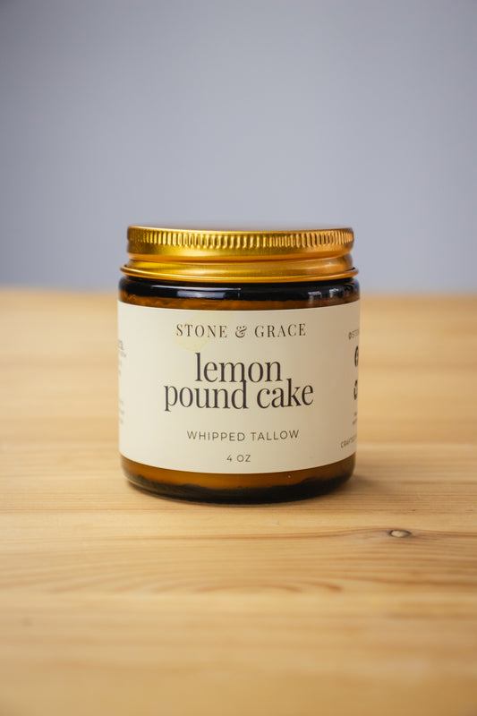 Jar of 'Lemon Pound Cake' whipped tallow from Stone & Grace on a wooden surface with a gray background