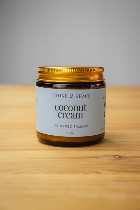 Jar of Stone & Grace coconut cream whipped tallow on a wooden surface with a gray background