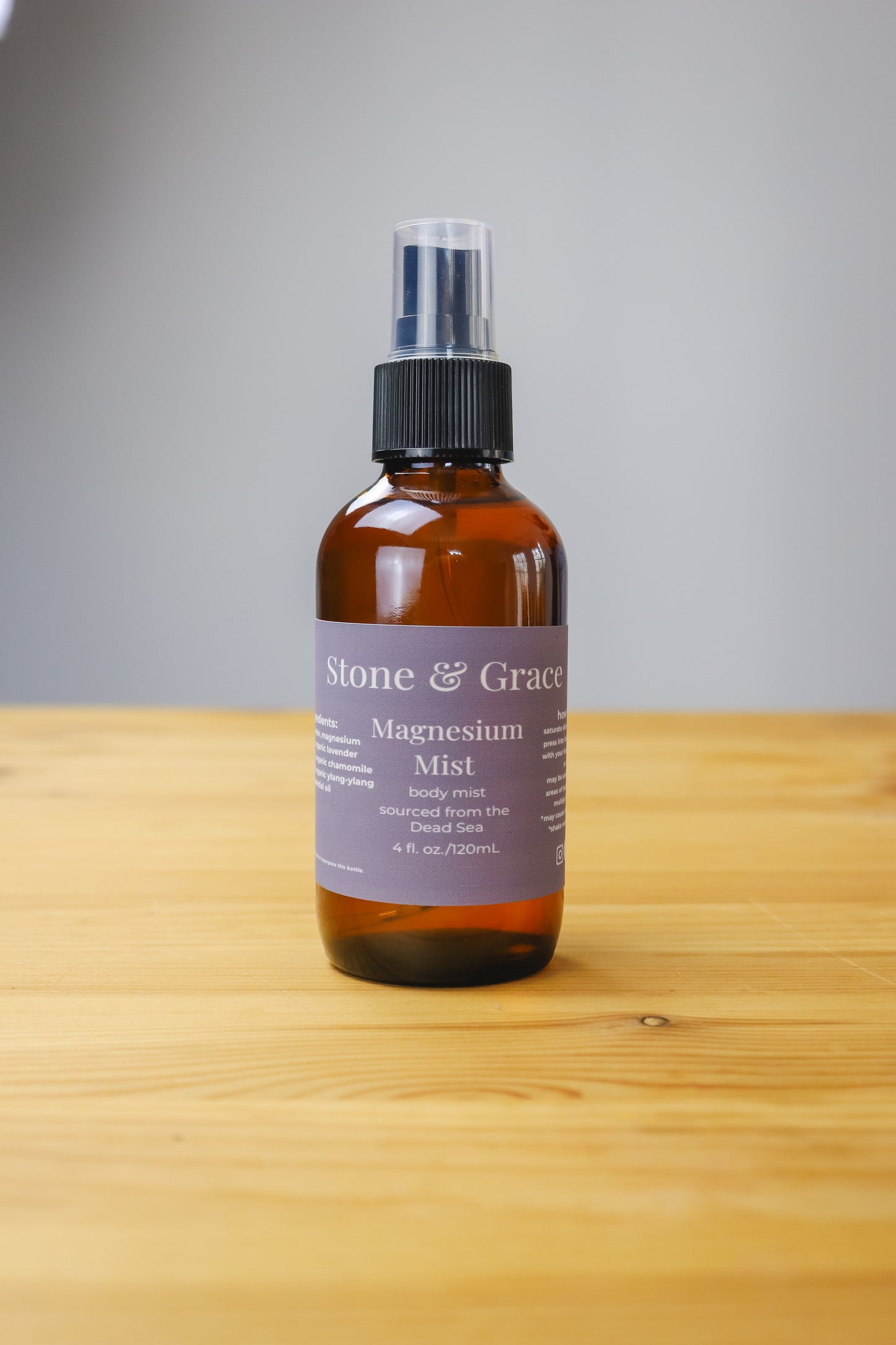 Bottle of Stone & Grace Magnesium Mist on a wooden surface with a gray background