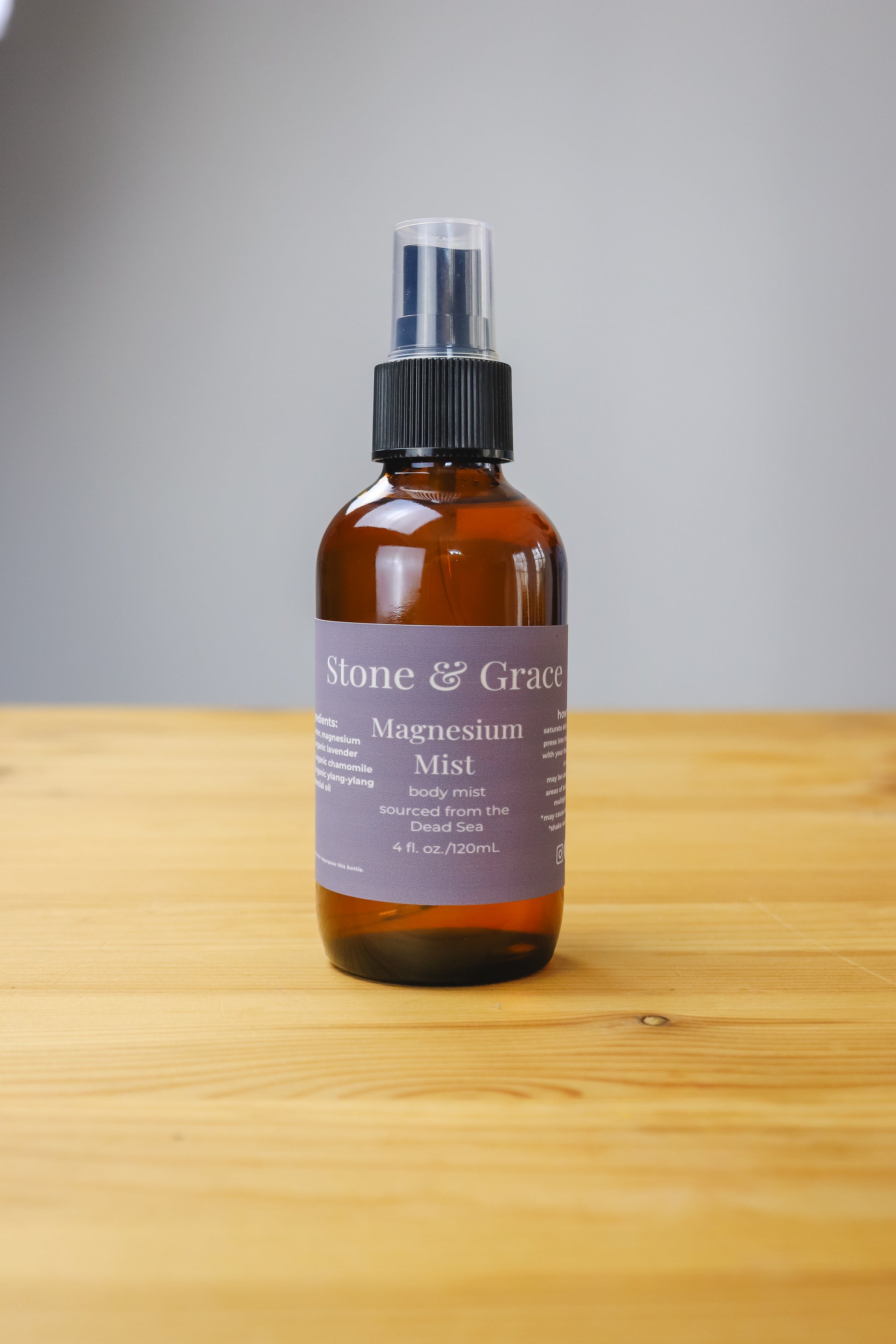 Bottle of Stone & Grace Magnesium Mist on a wooden surface with a gray background