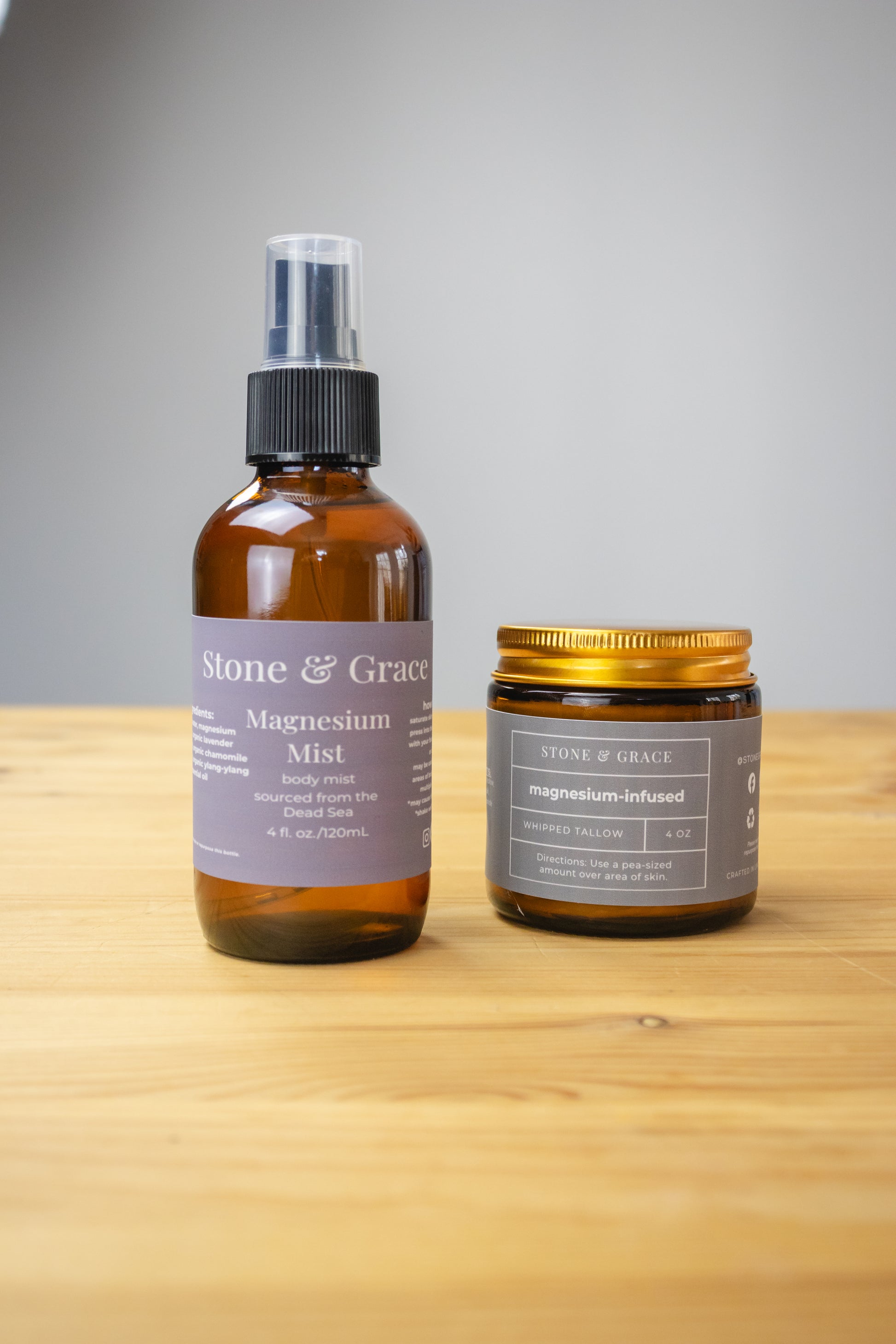 Two bottles of Stone & Grace products on a wooden surface with a gray background. Products include magnesium mist and magnesium-infused whipped tallow.