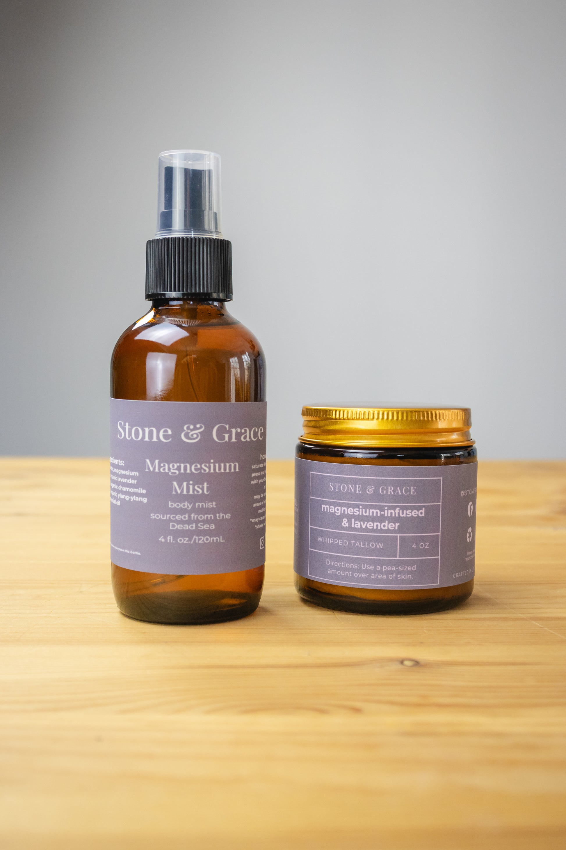 Two products from Stone & Grace on a wooden surface with a gray background. Products are Magnesium Mist and Magnesium-infused and lavender whipped tallow.