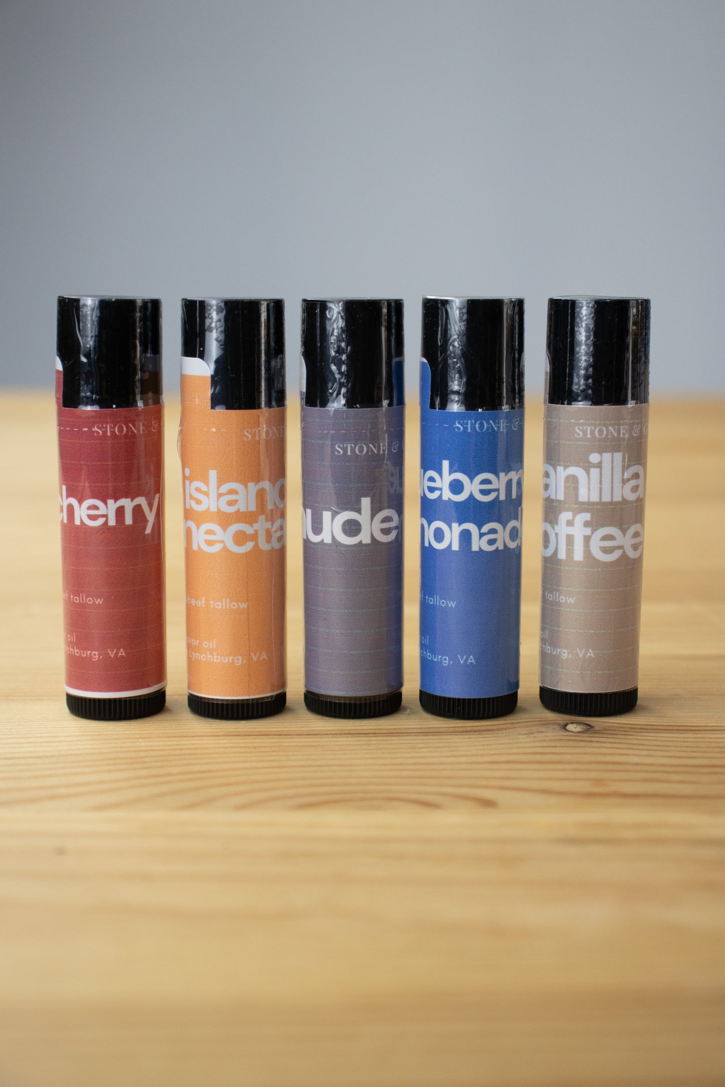 Five lip balm tubes with different flavors on a wooden surface