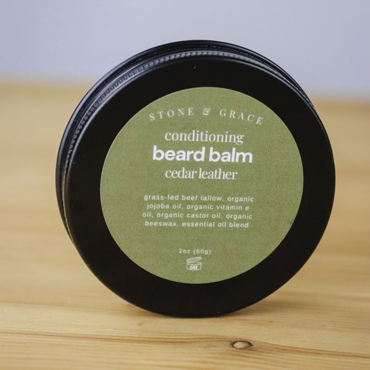 Container of Stone & Grace conditioning beard balm in 'cedar leather' scent on a wooden surface